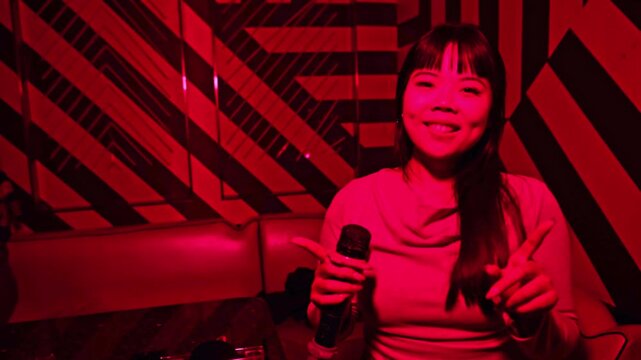 Asian woman singing karaoke in a red lit nightclub