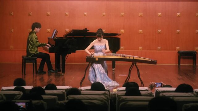 Asian musicians performing a duet with traditional and classical instruments on stage for an audience