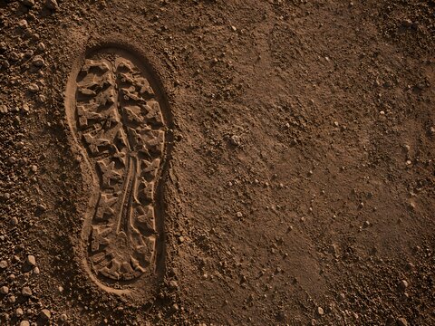 Top view of clear boot footprint imprint in red brown soil dirt ground texture with copy space