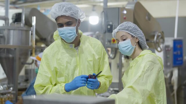Food factory automated production line, Sterile factory worker inspection production line cleanroom with protective suit and face mask, industrial safety uniform and blue glove quality control