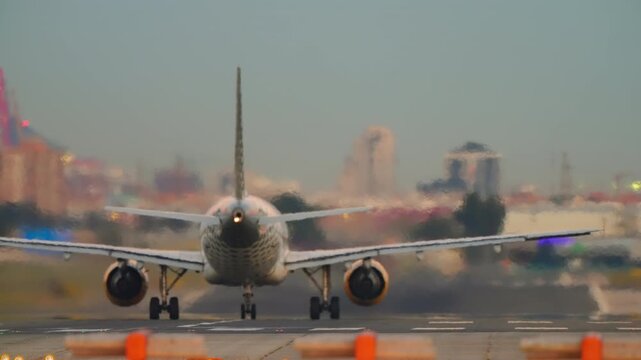 Close rear view of a narrow-body commercial jet on the runway at dusk, heat shimmer blurring the urban skyline while out-of-focus amber runway lights create golden bokeh across the foreground