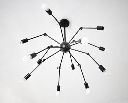 Bottom view of a modern black spider chandelier with adjustable arms and LED bulbs on a white ceiling.