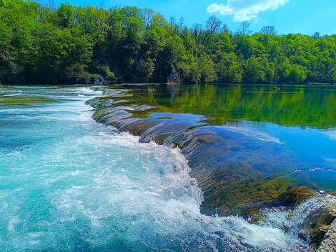 River with clean water and waterfalls in magnificent green nature with trees and blue sky