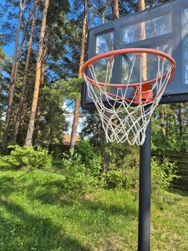 Basketball hoop standing outdoors under a bright blue sky surrounded by green summer nature. Active lifestyle concept about outdoor recreation, freedom and healthy suburban living.