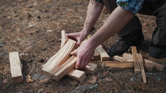 Male traveler arranging firewood on forest ground near camping campsite. Camper preparing wooden logs for campfire during outdoor hiking adventure in woodland nature. Recreation outdoors.