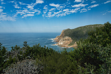 Fototapeta premium A scenic coastal view featuring a rocky cliff, calm ocean waters, and a clear blue sky with scattered clouds.