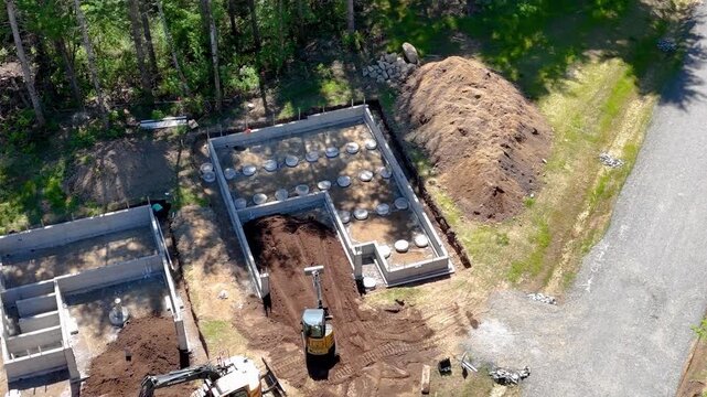 Aerial circling view of a mini excavator grading soil within a residential concrete foundation
