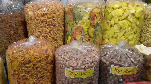 Cashew and macadamia nuts, dried mango, papaya and jackfruit together with other dried snacks are sold in large transparent plastic packs on the night market in Da Lat, Vietnam
