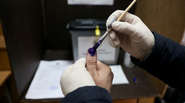 A person's finger being marked with indelible ink by a poll worker wearing gloves at an election booth.