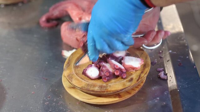 Professional chef's hands with blue gloves cutting boiled octopus tentacles with scissors. Preparing a traditional spanish seafood tapas dish