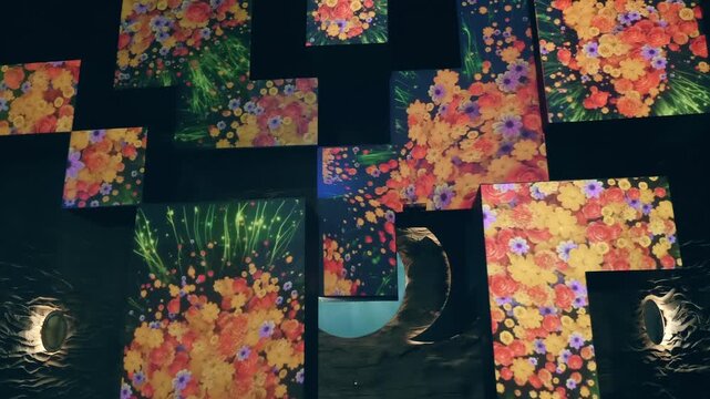 Big rectangular, square and L-shape panels hang in the air in the dark room with colorful flowers being projected on them. A fairy tale visual light installation