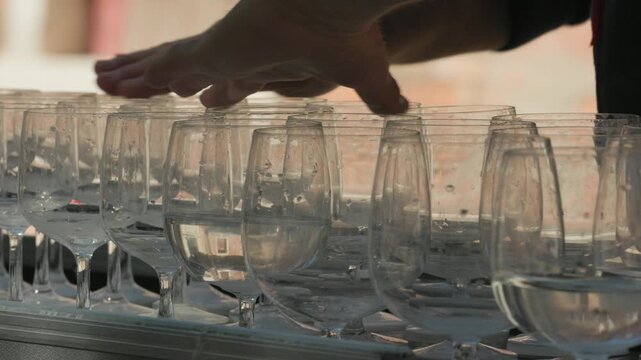Close up of a street musician playing a glass harp. The performer's hands hover and rub the wet rims of crystal wine glasses filled with water to create acoustic music outdoors in the city