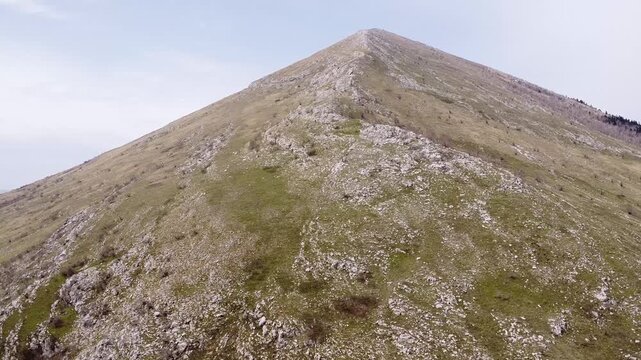 Stunning aerial view of a majestic and remote mountain peak Rtanj, Serbia. The drone smoothly glides over the rocky and grassy slope toward the summit