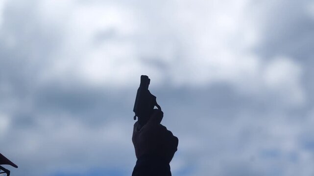 A starter's hand fires a blank pistol into the cloudy blue sky