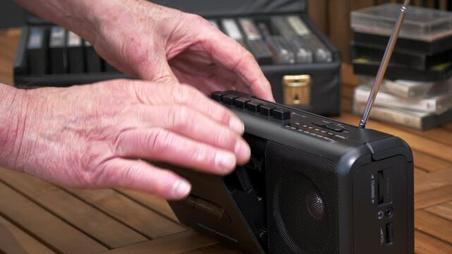 Closeup of a senior man&rsquo;s hand taking an audio cassette tape out of its case, from a collection, then inserting it into a portable player and pressing the play button to listen.