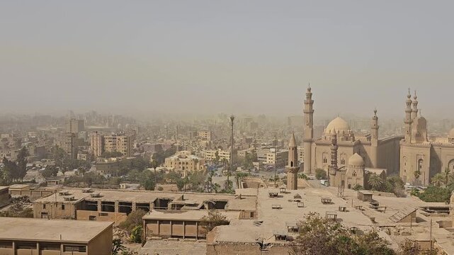 Dusty atmospheric skyline of Cairo, Egypt, dominated by the medieval Sultan Hassan and Al-Rifa'i mosque complex, featuring tall minarets, stone domes and ornate facades.