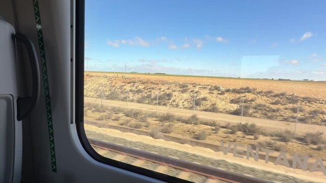 Passenger's point of view from a train window looking out at a fast-moving rural landscape
