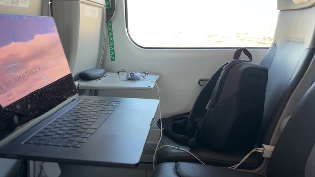 Digital nomad lifestyle with a laptop and backpack inside a moving train while looking at the scenery