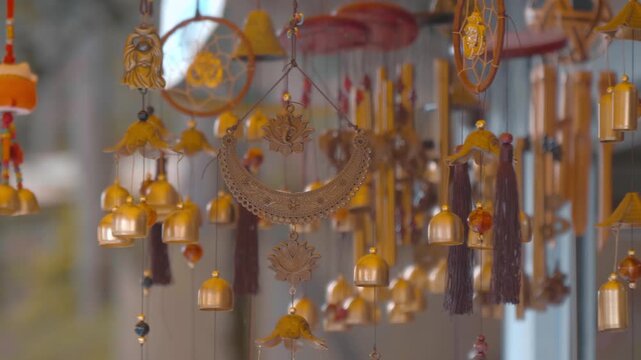A multitude of shiny gilded tubular wind chimes with bells and engraved Hindu Om signs hang in a row and sway in the wind, producing melodic sounds
