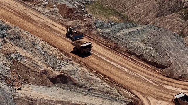 Aerial of dump trucks and tractors in mine pit in high desert area in utah