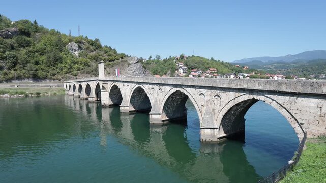 Visegrad, Bosnia and Herzegovina - August 10, 2025: Scenic view of medieval stone arched Mehmed Pasa Sokolovic Bridge spanning Drina River on sunny summer day