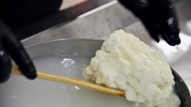 Hand stirring and pulling fresh stracciatella cheese from boiling water