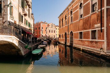 Obraz premium Sunny Venetian Canal With Traditional Stone Bridge and Old Buildings