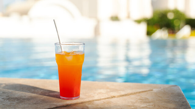 Bright orange drink with ice sits poolside