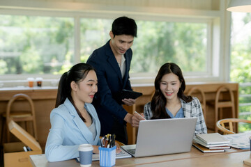 Obraz premium Asian business team collaborating, discussing ideas, and working together on a laptop in a contemporary office environment