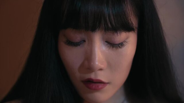Extreme close up of a depressed and heartbroken young asian woman crying in a dark room