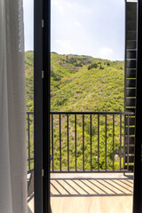 Fototapeta premium Balcony view of green hills through open glass door