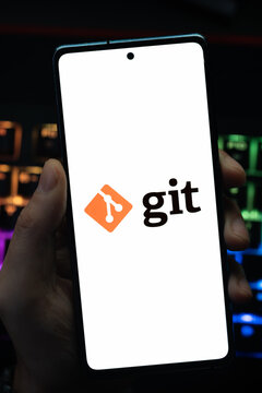 Punta Arenas, Chile &ndash; May 18, 2026: A person holding a smartphone that displays the Git software logo on its screen, with a blurry RGB backlit keyboard in the background