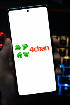 Punta Arenas, Chile &ndash; May 18, 2026: A person holding a smartphone that displays the 4chan imageboard website logo on its screen, with a blurry multi-colored backlit keyboard in the background