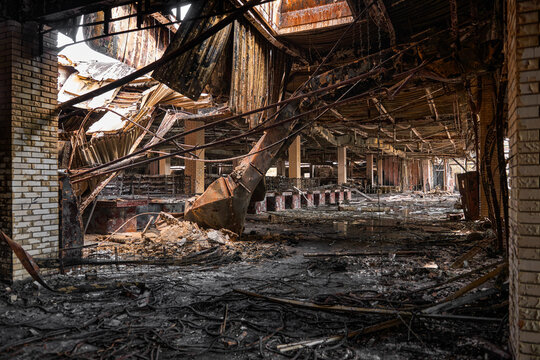 Charred metal structures and debris litter the floor of a large commercial building following fire damage. Burnt ceiling panels and twisted wires highlight the scale of the destruction.