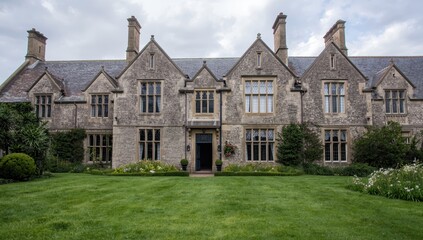 Fototapeta premium Imposing, aged stone mansion featuring intricate gables, chimneys, and divided windows, enveloped by vibrant gardens in gentle, cloudy light in Trerice - Newquay - Cornwall - UK.