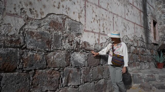 Mature woman explores the historic wall of Mission Church in San Ignacio while looking at the stonework in Baja California Mexico