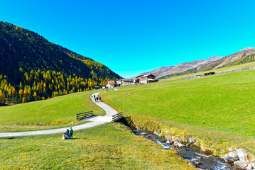 Malerischer Wanderweg mit Holzbrücke und Alpendorf im herbstlichen Langtauferer Tal in Südtirol © Ilhan Balta
