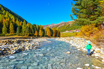 Kind am Ufer des Karlinbachs mit Blick auf herbstliche Lärchenwälder im Langtauferer Tal, Südtirol  © Ilhan Balta