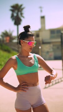 Energetic female jogger taking break on sunlit seaside promenade