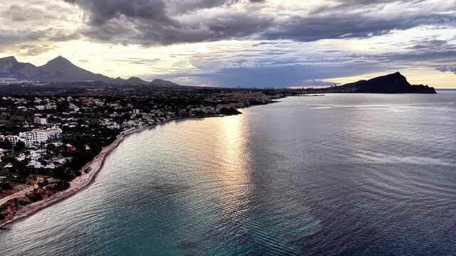 Aerial resort coastline at sunset, golden turquoise shallows beachfront promenade cluster of buildings,