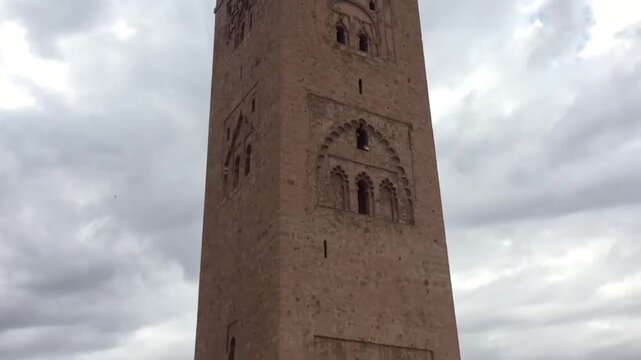 Cinematic slow pan of Koutoubia Mosque minaret beneath dramatic cloudy sky in Marrakech