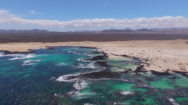 Aerial view of coastline from the Classic, candy-striped Toston lighthouse which is stands on the volcanic beach. Drone POV exploration of Fuerteventura Island. Volcanic beach view.