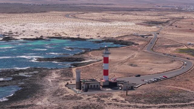 Aerial view of coastline from the Classic, candy-striped Toston lighthouse which is stands on the volcanic beach. Drone POV exploration of Fuerteventura Island. Lighthouse view.