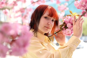 Fototapeta premium Beautiful young girl posing near blossoming sakura tree outdoors