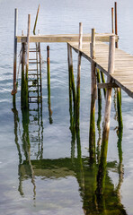 Fototapeta premium Old wooden pier and jetty on stilts with algae-covered poles over calm water, Ria de Aveiro, Portugal