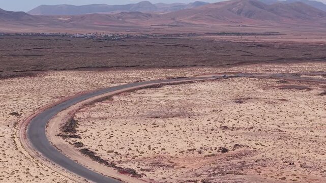 Aerial view of coastline from the Classic, candy-striped Toston lighthouse which is stands on the volcanic beach. Drone POV exploration of Fuerteventura Island. Road view with the moving cars.