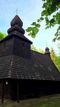 Traditional wooden church in Slovakia with shingle roof and spring green trees