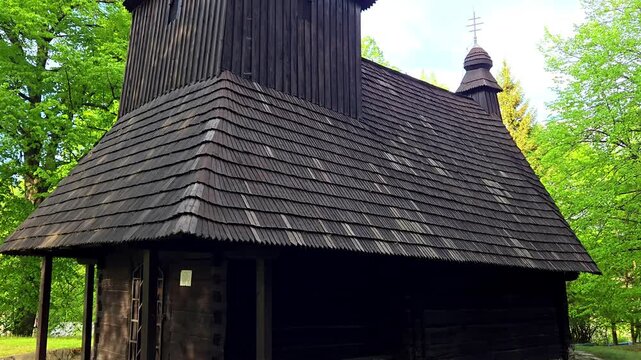 Traditional wooden church in Slovakia with shingle roof and spring green trees