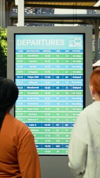 Multicultural group of passengers waiting before interstate coach departure, inside regional bus hub. Travelers group with carry-on luggage checking departure board, long-haul relocation travel.