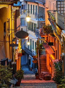 Bellagio village at lake Como near Milan Italy, region Lombardy. Night view of famous street with paving stones stairs and cosy restaurants during sunrise with glowing lanterns and old houses walls.